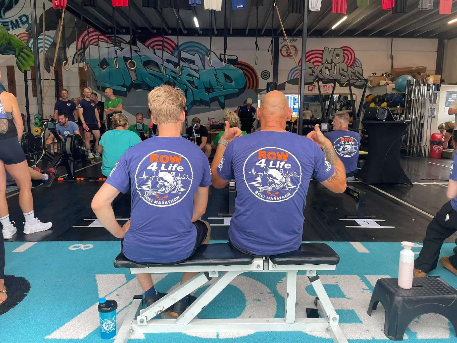 Twee deelnemers in Row 4 Life-shirts kijken toe vanaf de bank