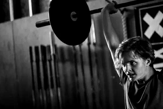Tiener drukt een barbell boven het hoofd tijdens WOD Teens